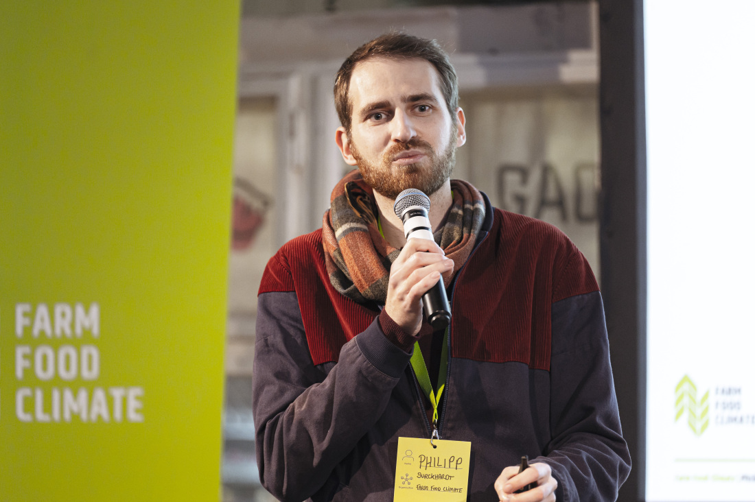 Philipp Burckhardt mit Mikrofon vor dem Farm Food Climate Logo