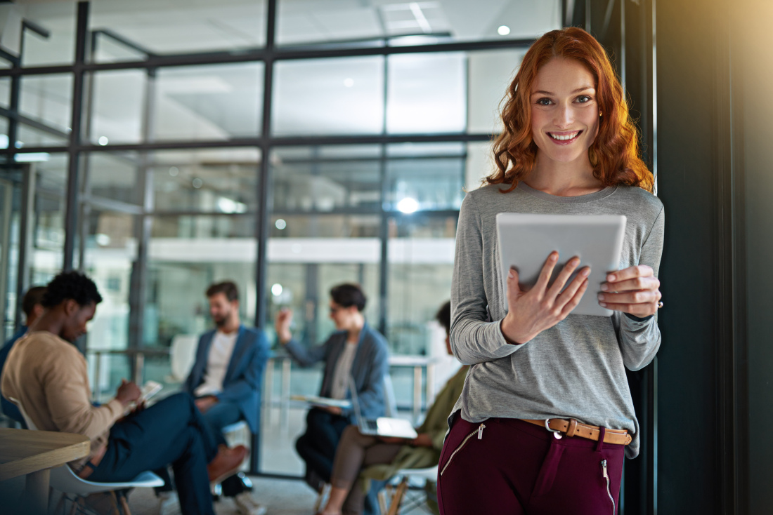 A woman is standing in the front with a tablet in her hands, looking into the camera.