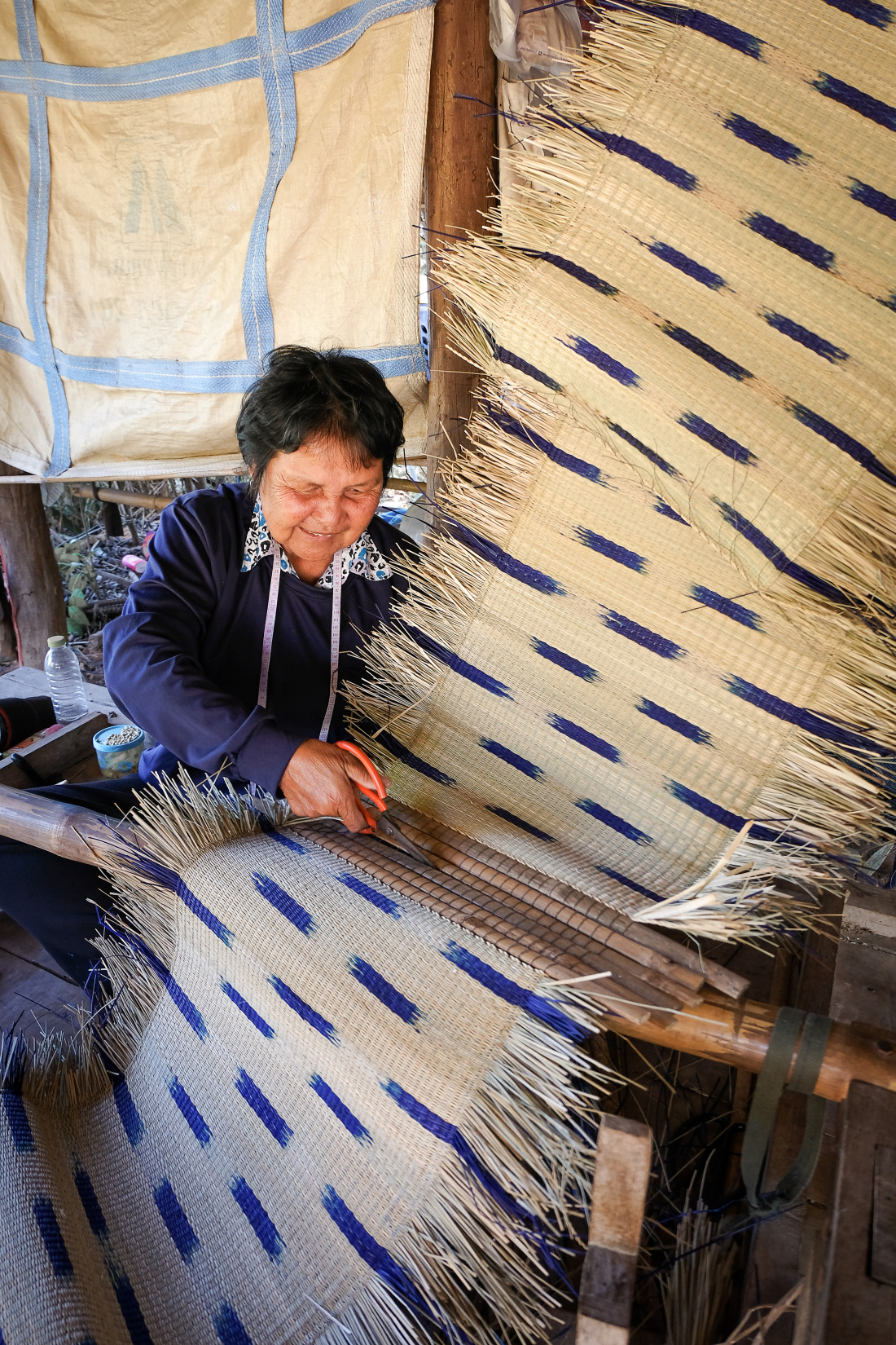 Eine thailändische Frau schneidet einen geflochtenen Teppich zu