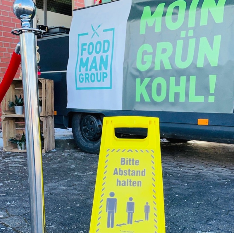 Gelbes Schild mit der Aufschrift "Bitte Abstand halten" vor dem Foodtruck