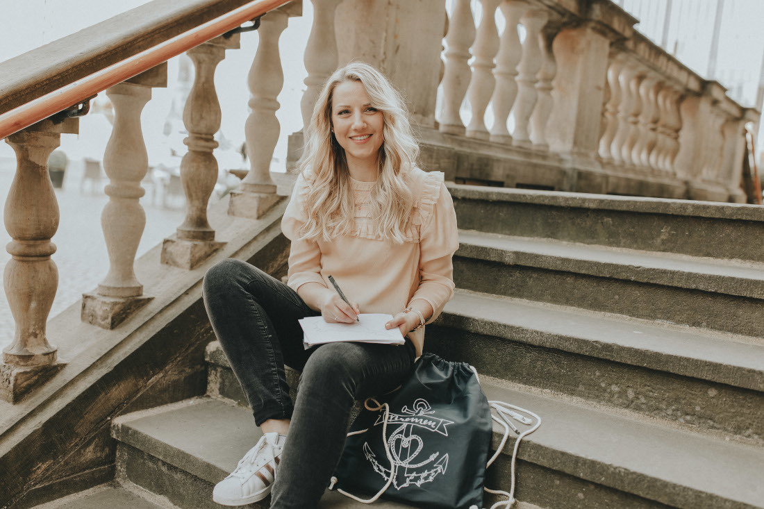 Ann-Kristin Riemann sitzt auf einer Treppe und schreibt.