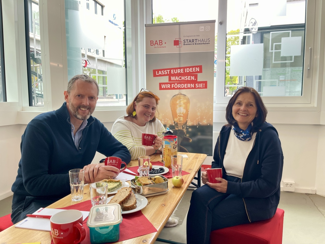  3 Mitarbeiter*innen vom Starthaus sitzen an einem gedeckten Mittagstisch 