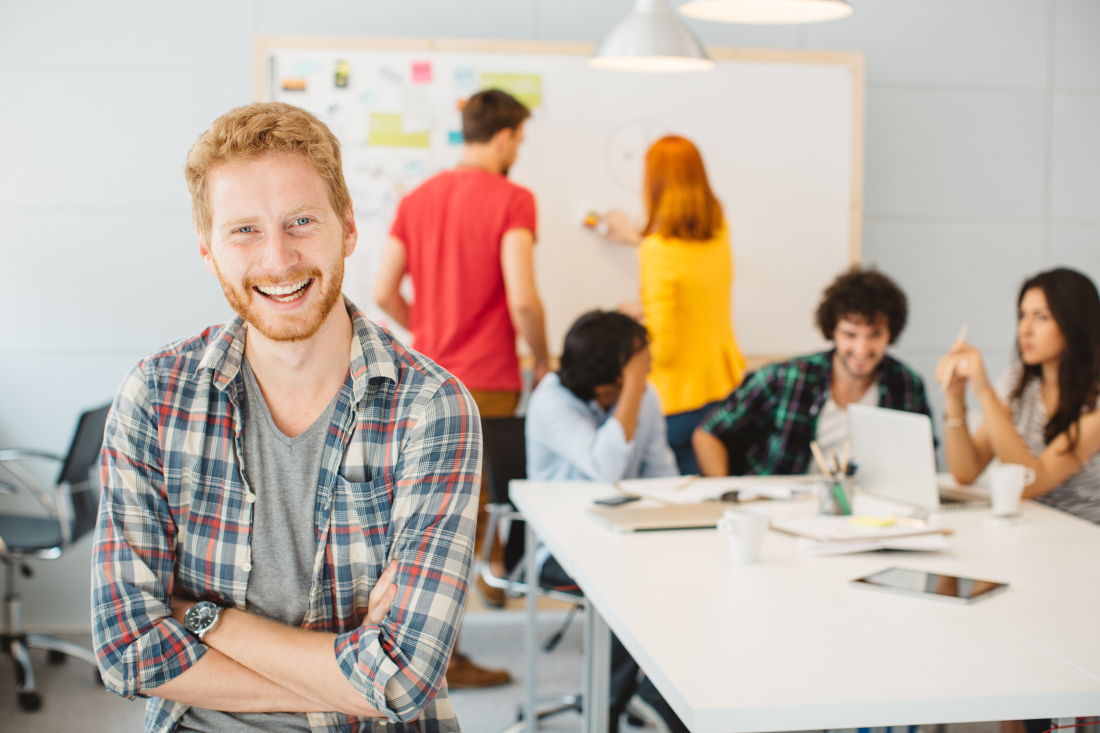 Ein Mann schaut in die Kamera, im Hintergrund findet ein Workshop statt