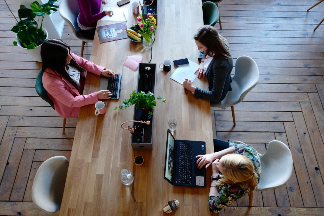 Three women working on their laptops at one large desk