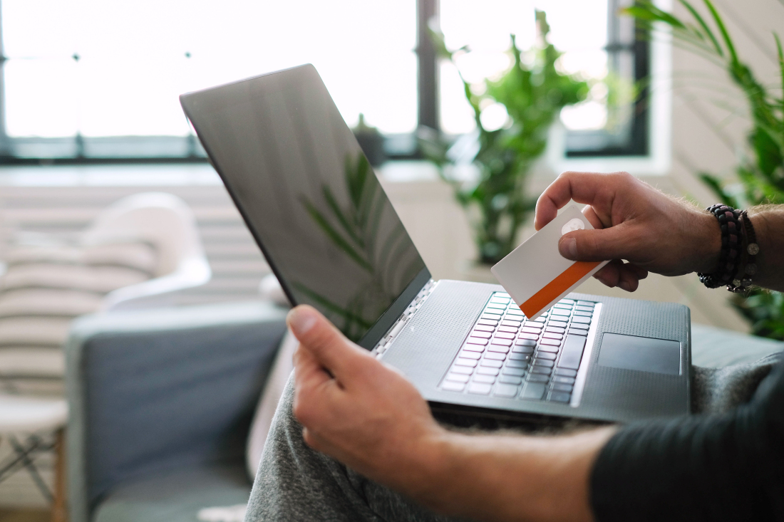 Ein Laptop auf dem Schoß und eine Kreditkarte in der Hand